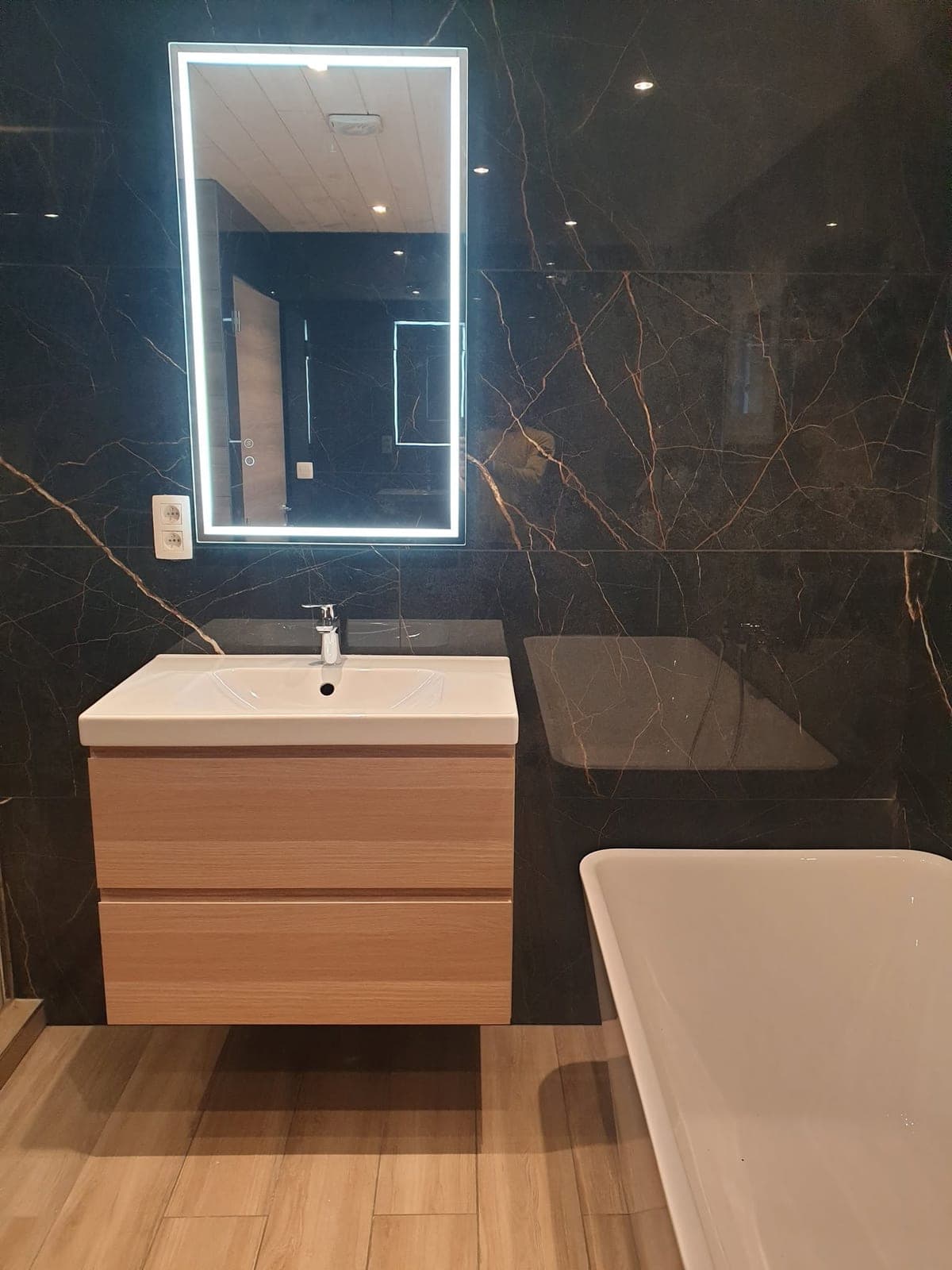 Meuble vasque suspendu, miroir éclairé et baignoire sur fond sombre